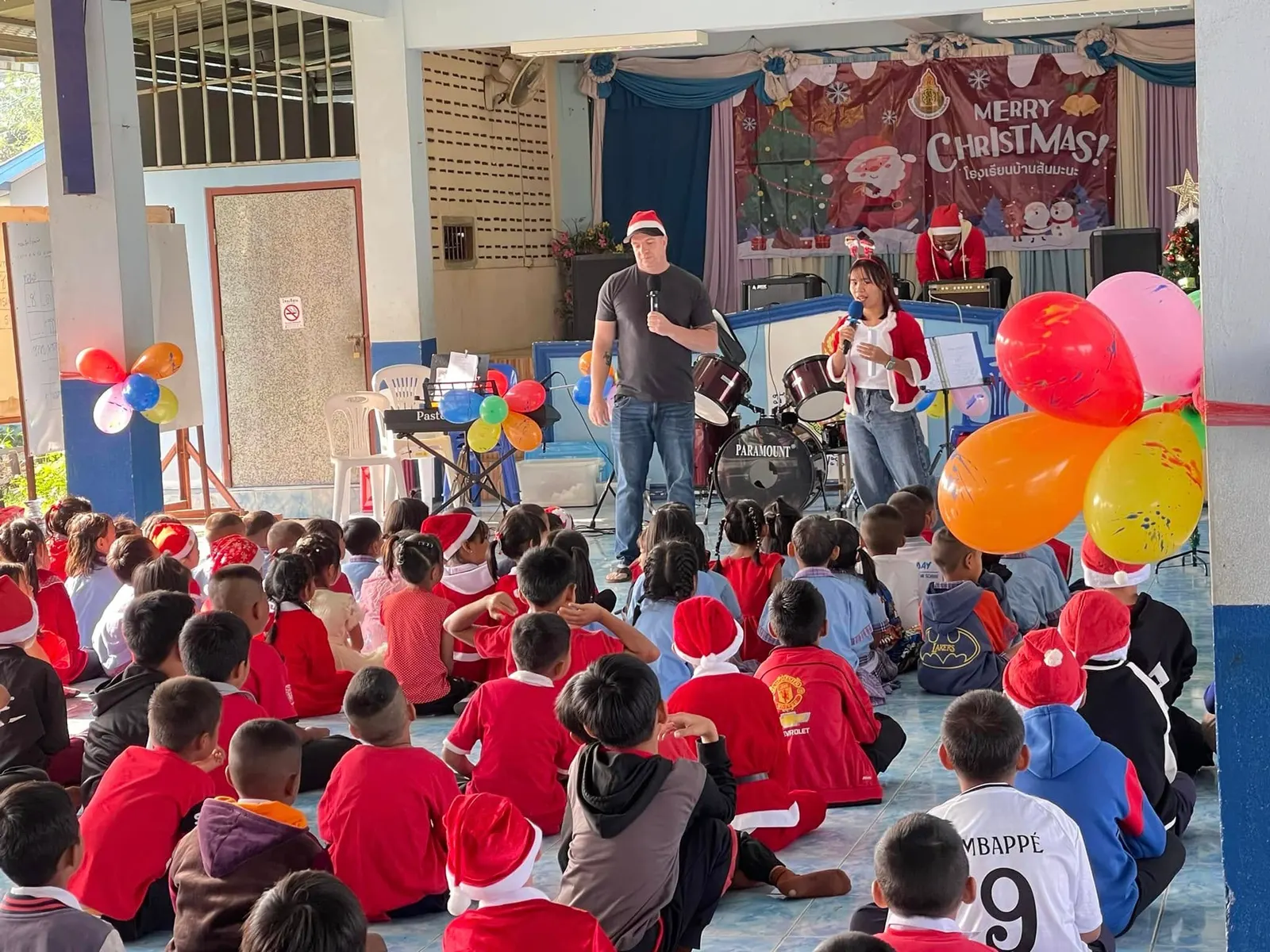 Children in Santa hats watch a Christmas programme with balloons and music at a Mae Sai school