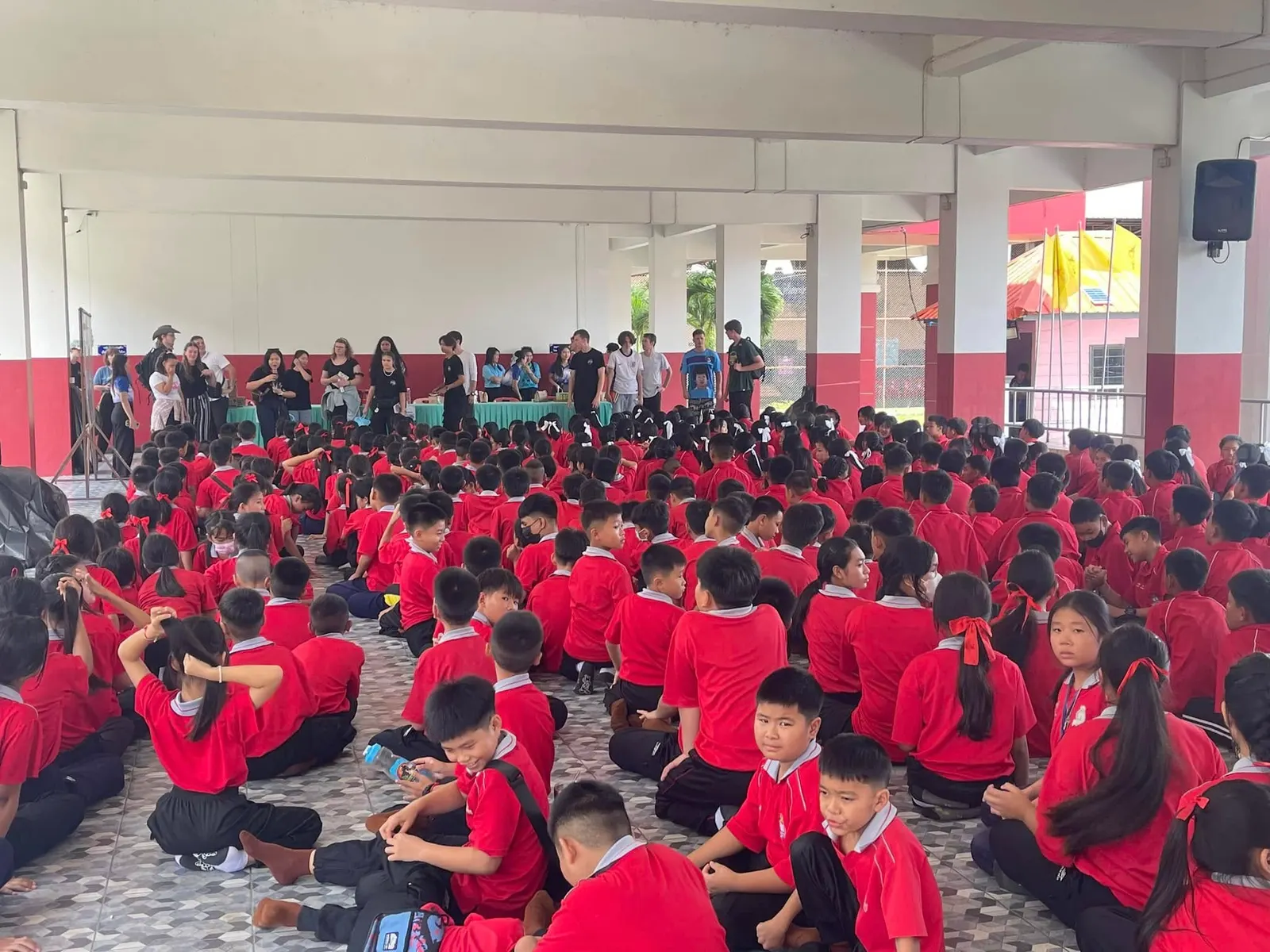 Hundreds of students in red shirts sit on the floor of a school hall in Mae Sai during a visit by a volunteer team