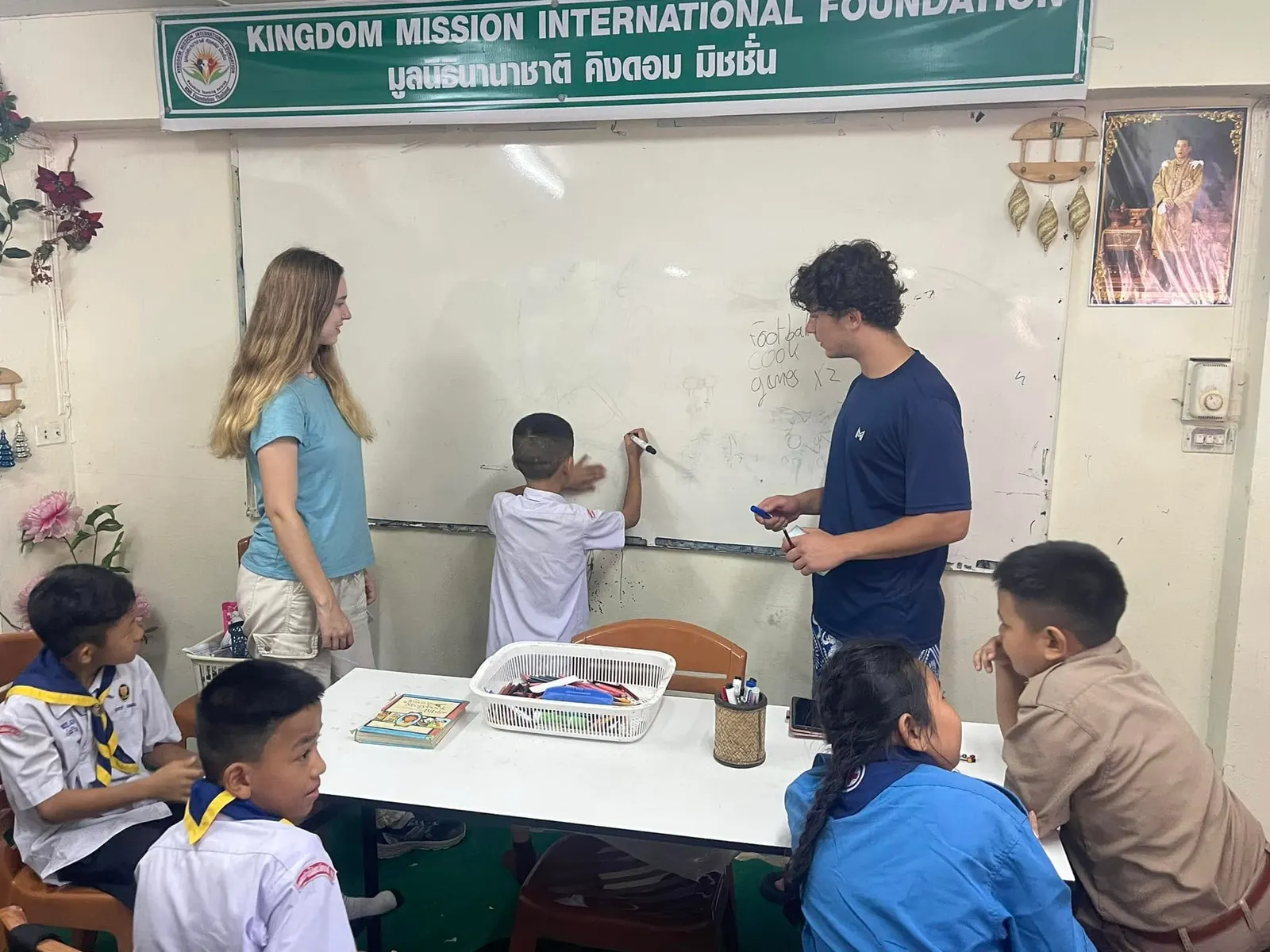 Two international volunteers teach English at the whiteboard in the KMI-Foundation Thailand classroom in Mae Sai